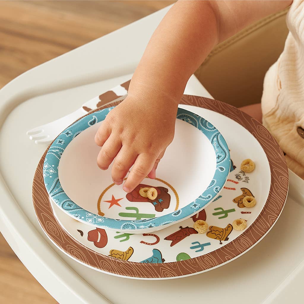Children's dinnerware set with cowboy-themed plates, bowl, and cutlery on a white background
