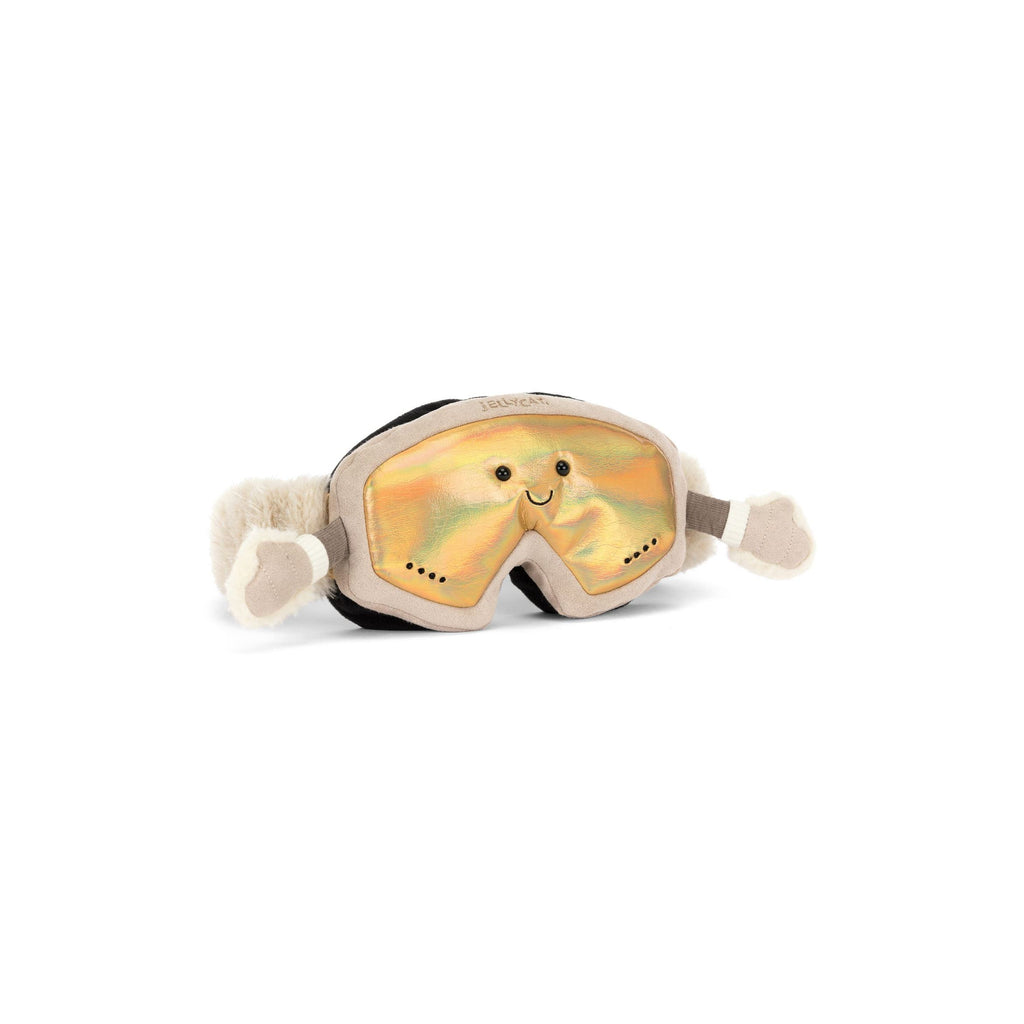 A plush toy snowboard goggles with a smiling face printed on the iridescent yellow lens, featuring a beige frame and white pom-pom ear covers on a white background.
