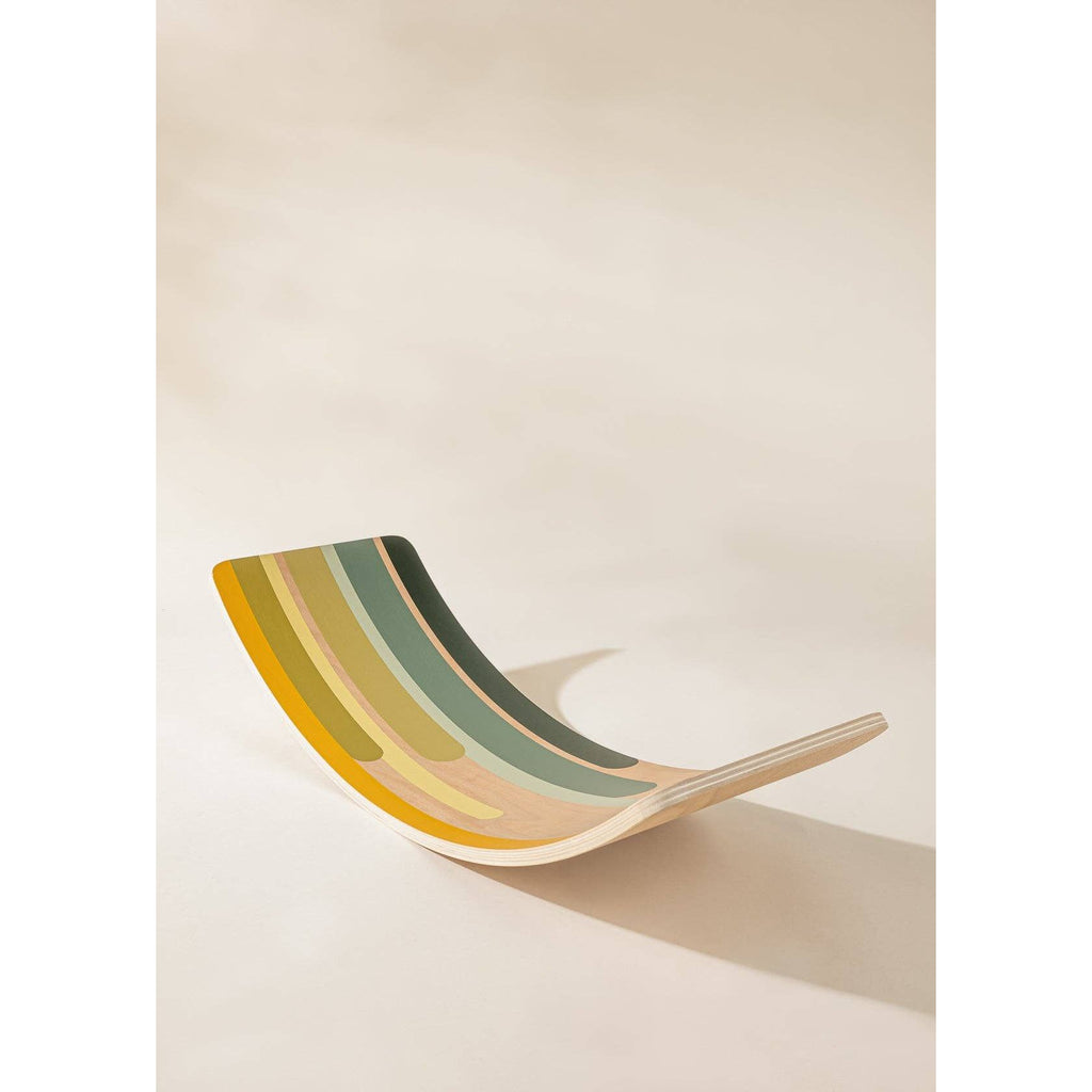 Child balancing on a colorful wooden balance board indoors.