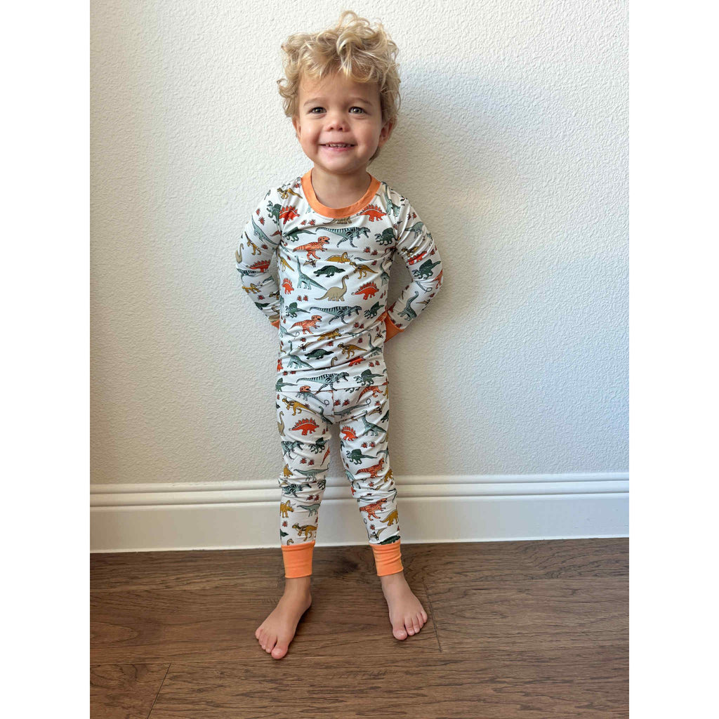 Child wearing dinosaur-themed pajamas standing against a plain wall.