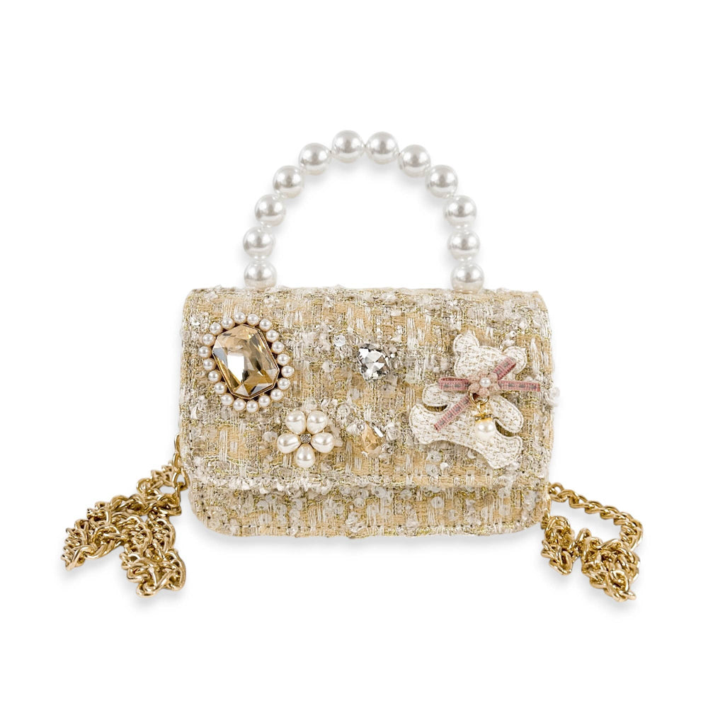 A miniature structured tweed handbag in beige and gold, embellished with faux pearls, crystals, and floral appliqués, featuring a pearl-beaded top handle on a white background.