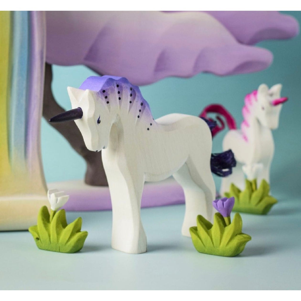 Wooden unicorn figurine with a purple mane on a wooden surface and light blue background