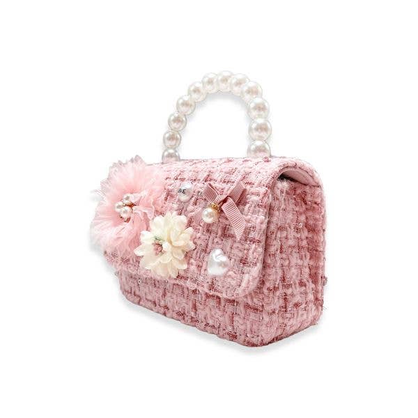 A pink tweed handbag with a pearl-bead handle, decorated with a large pink tulle flower, a white fabric flower, a pink ribbon bow, and a small pearl heart on a white background.