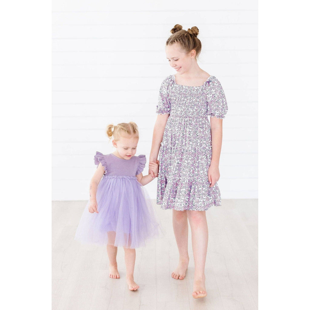 Child in a purple dress sitting on a chair with pink and white decor in the background