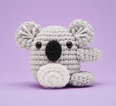 Crochet kit with a koala-themed product, including yarn, hooks, and packaging on a white background.