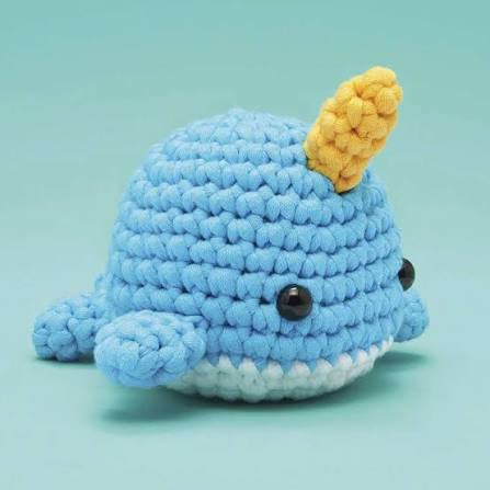 Crocheted blue whale toy with a yellow fin on a teal background