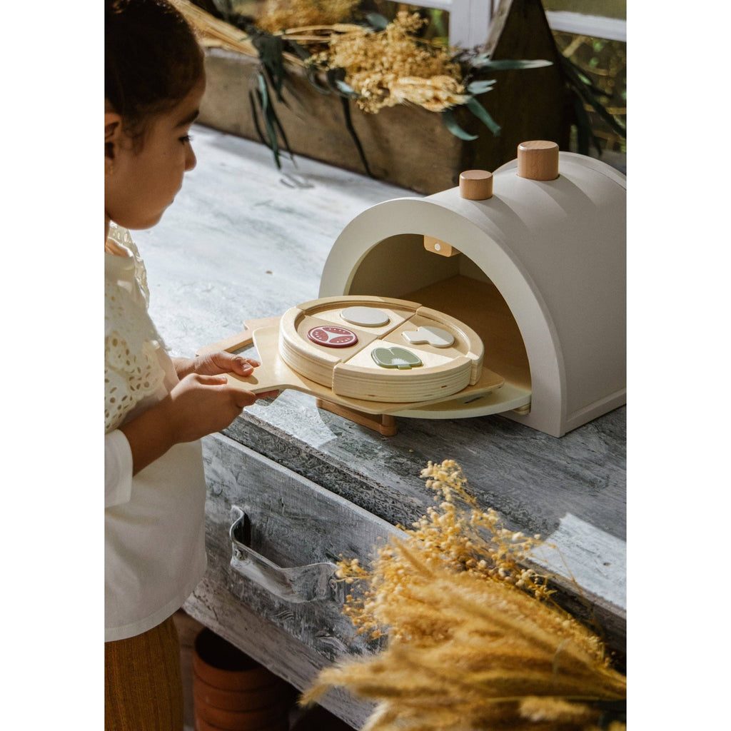 Wooden toy pizza oven with accessories on a light beige background