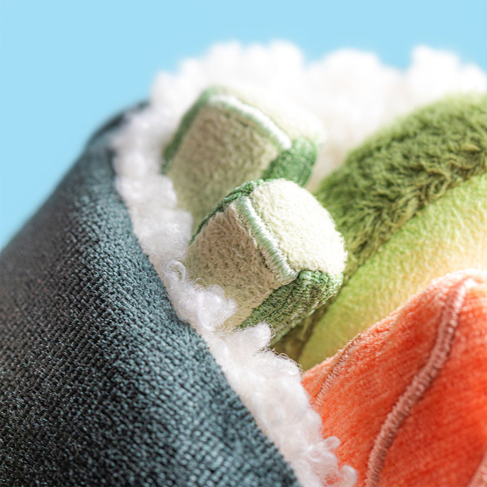 Stuffed toy resembling a sushi roll with black exterior, orange and green fillings on a white background