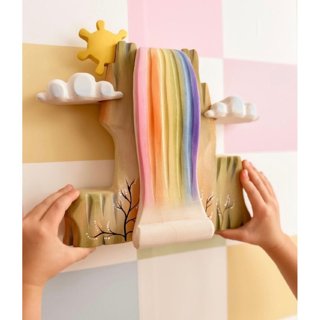 Wooden toy set with a rainbow waterfall, sun, and clouds on a light blue background.