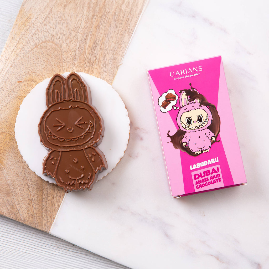 Chocolate cookie shaped like a character next to a pink Carians Labudabu packaging on a marble surface.