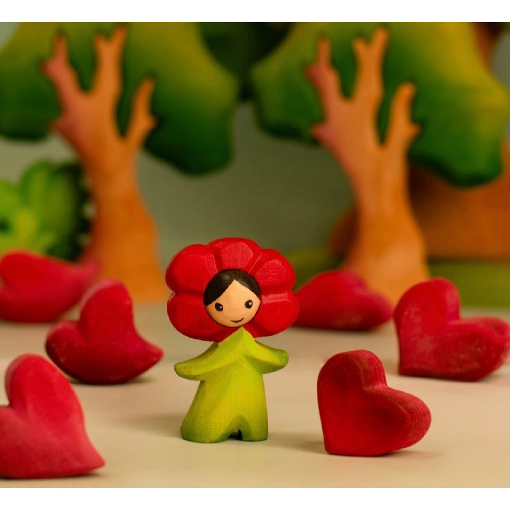Figurine with red flower head and green body on a wooden surface with light blue background
