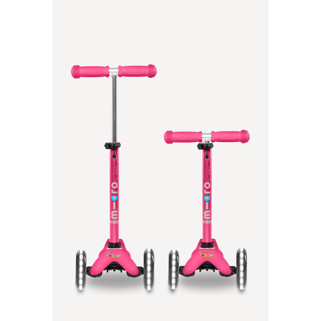 Child on a pink scooter wearing a helmet in a grassy outdoor setting