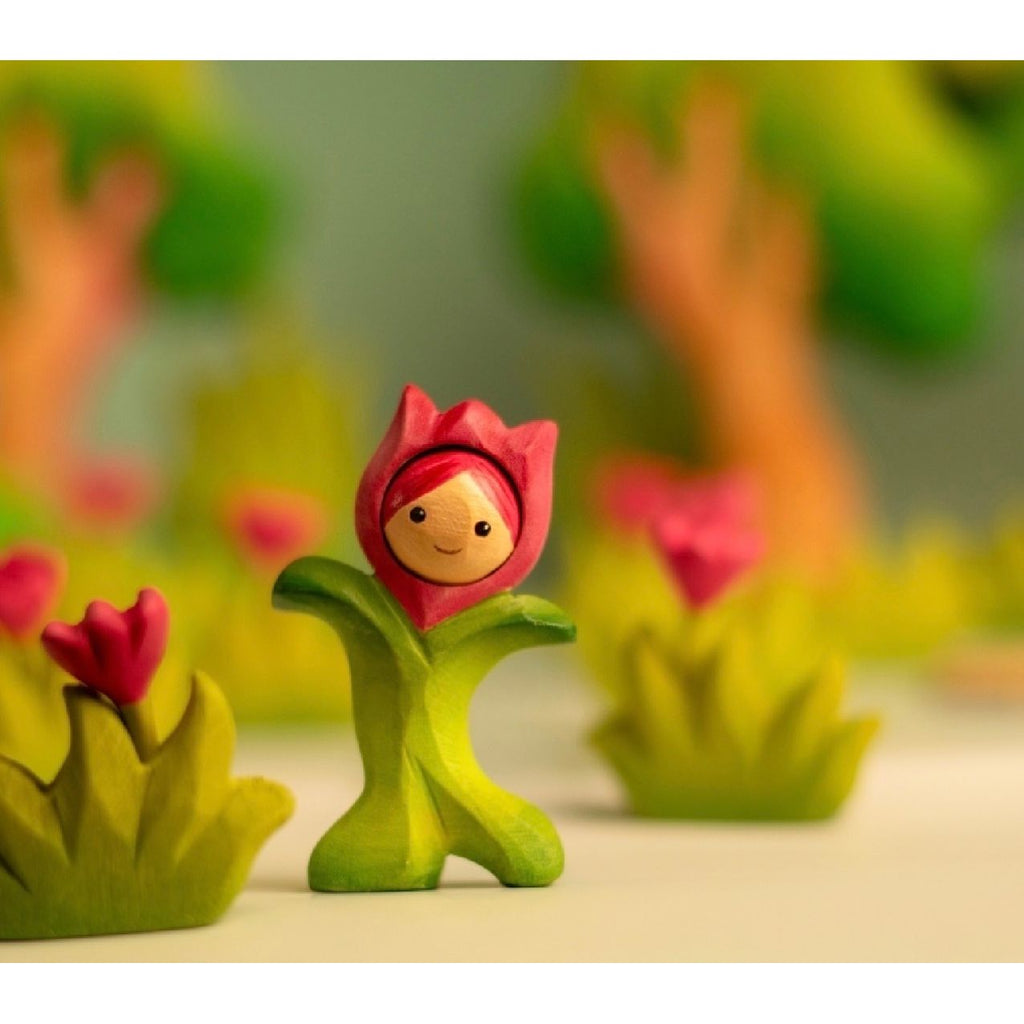 Toy figure of a girl with pink hair and green dress on a wooden surface with a light blue background