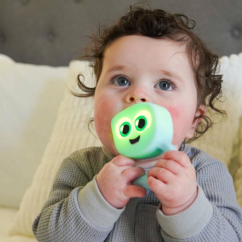 Baby holding a glowing green toy with a smiling face