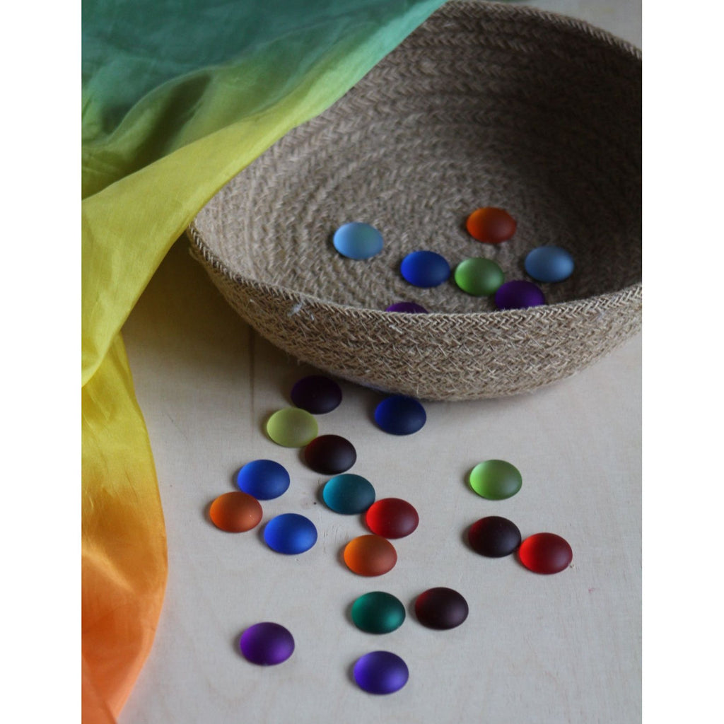 Colorful painted stones on a textured surface with a rainbow fabric in the background