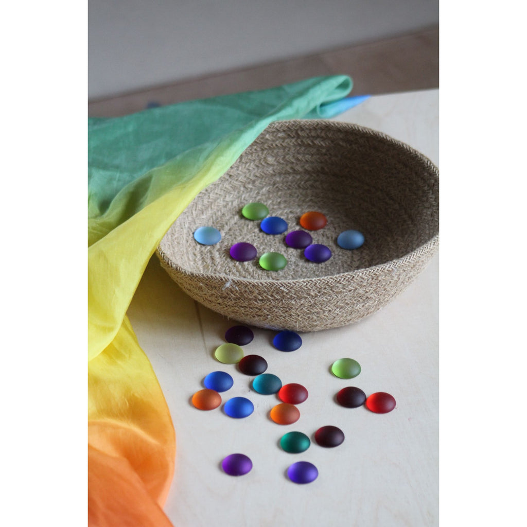 Colorful painted stones on a textured surface with a rainbow fabric in the background