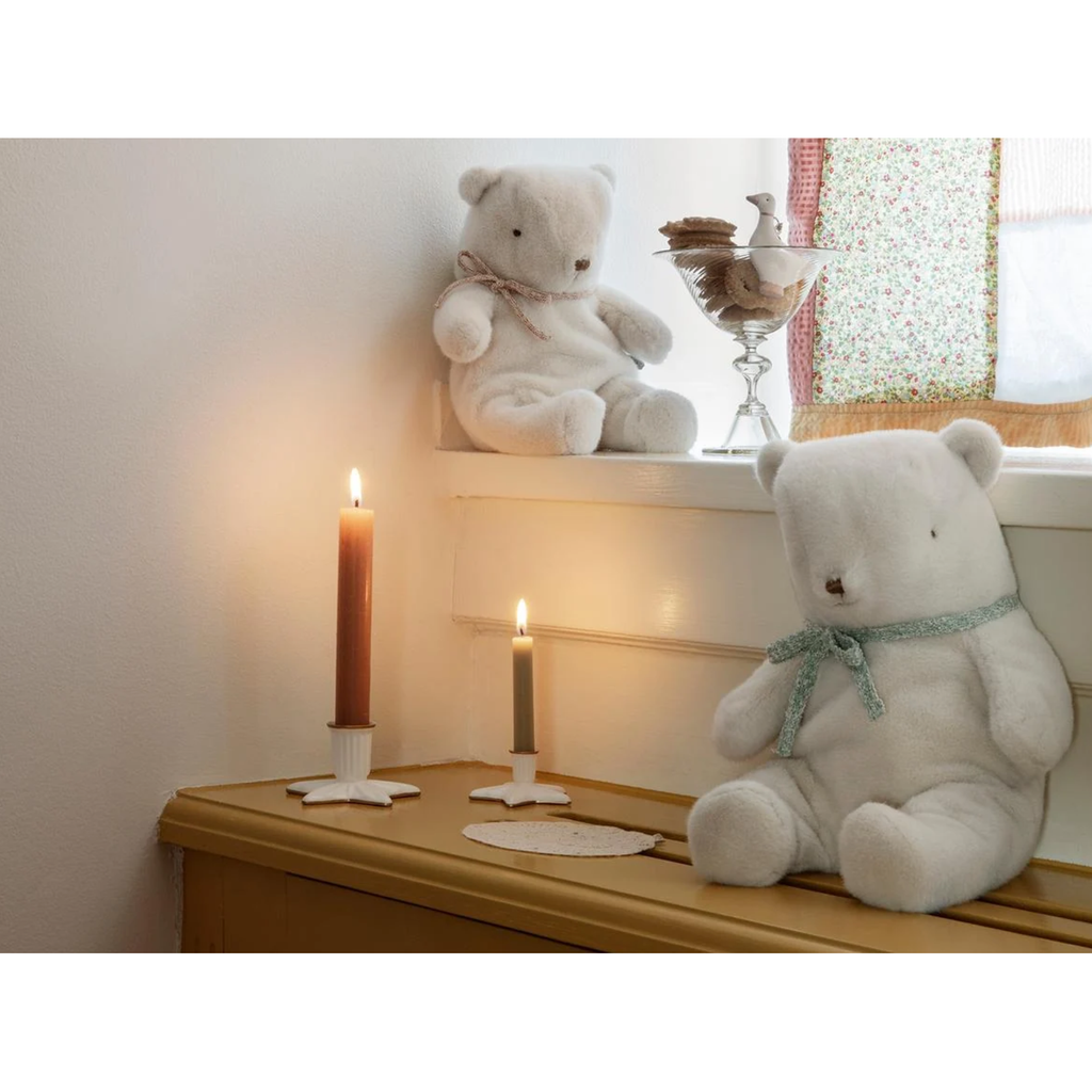 A cream-colored plush teddy bear with a mint green glittery bow around its neck.