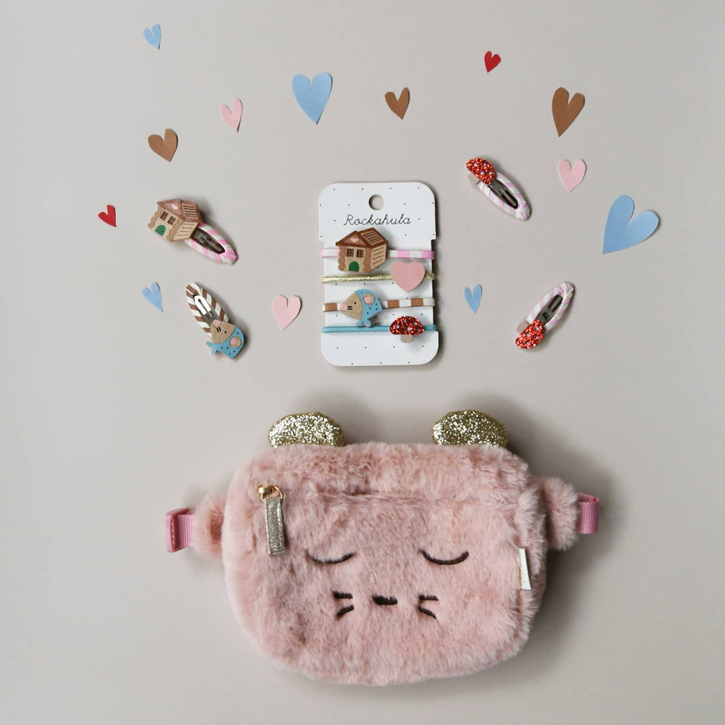 Pink fluffy pouch with decorative hair clips on a light gray background with heart shapes.