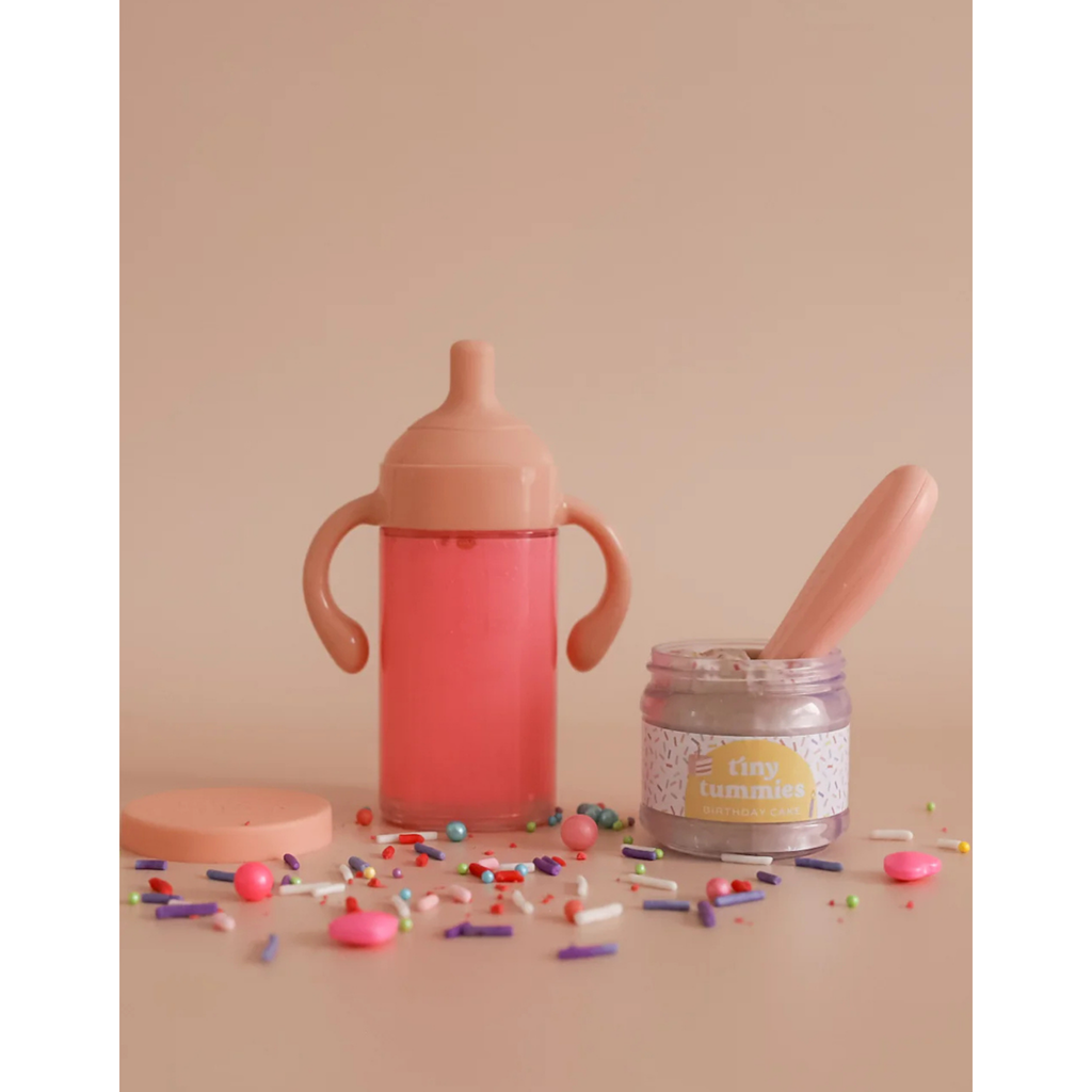 Pink sippy cup, jar with spoon, and colorful sprinkles on a beige background