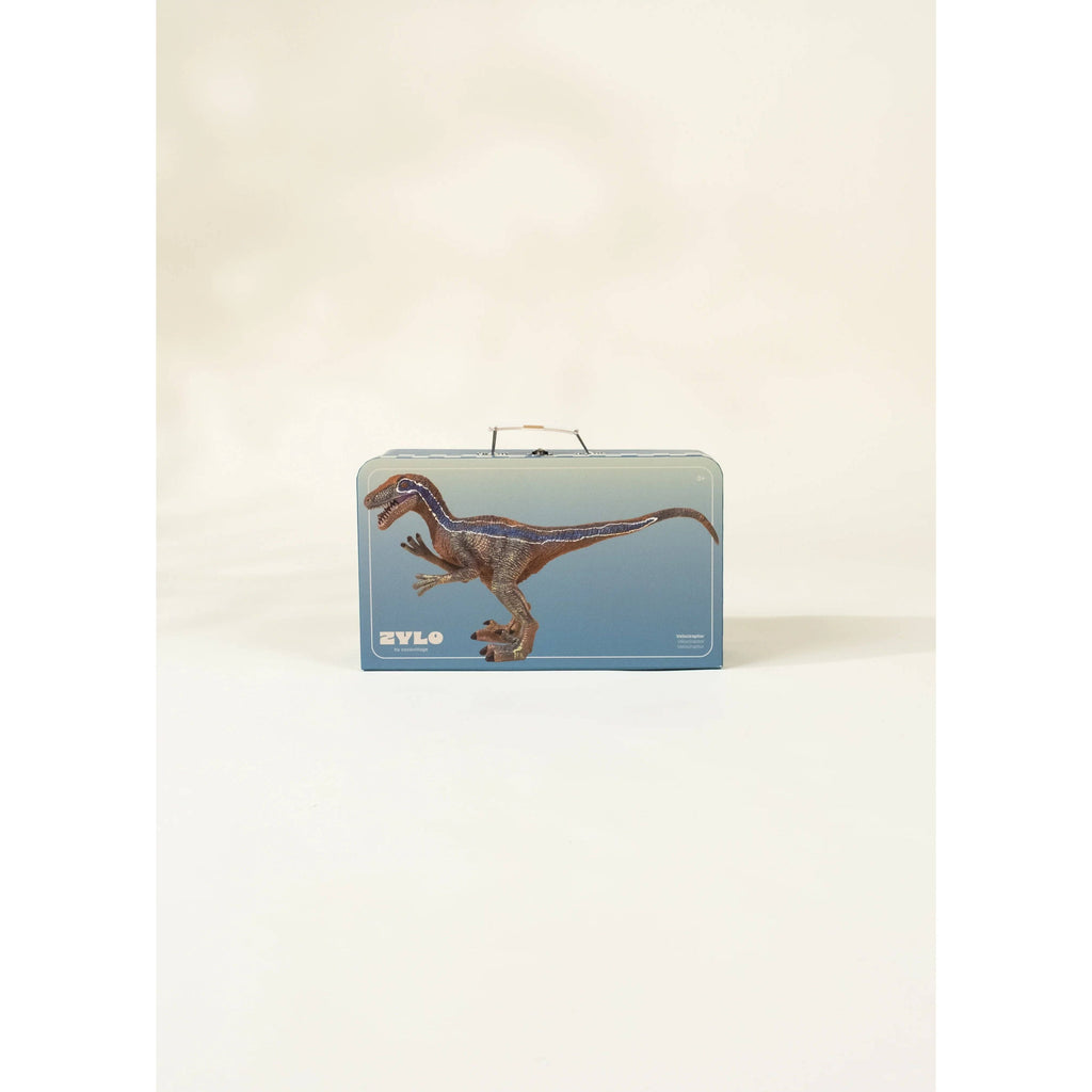 Toy dinosaur figure next to a blue suitcase with mountain design on a beige background