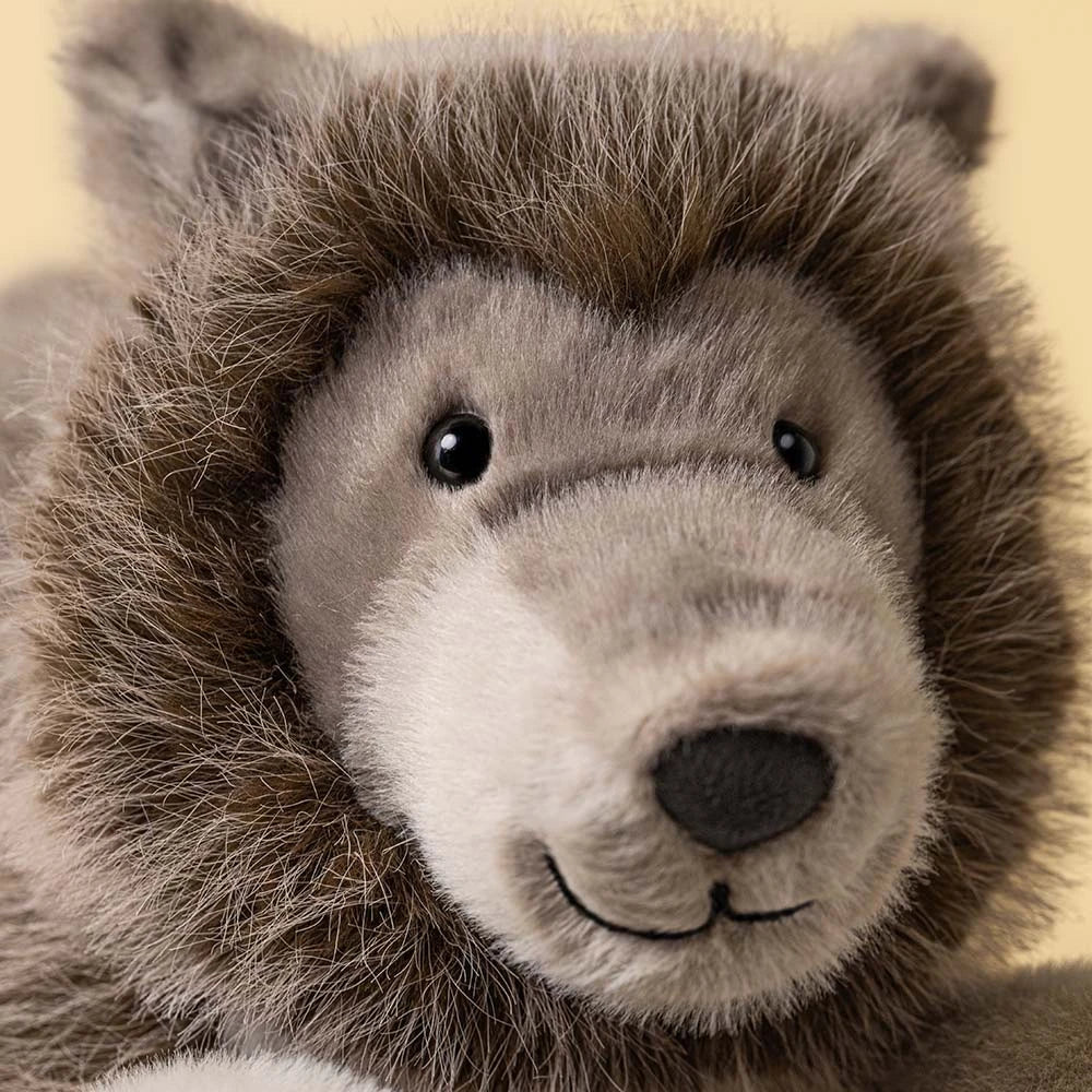 A plush stuffed animal shaped like a wolf or wild cat, lying down on a clean white background. The toy has a brown and gray body with a lighter beige muzzle and gray paws and legs.