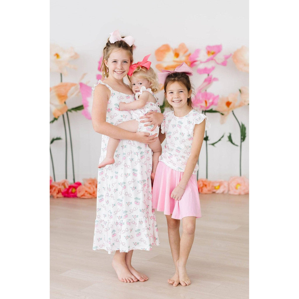 Child wearing a white sleeveless top with pink floral and bow pattern and a pink skirt.