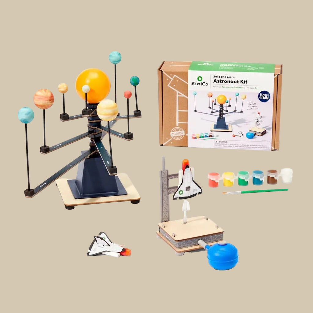 Educational astronomy model kit with planets, space shuttle, and painting supplies on a beige background.