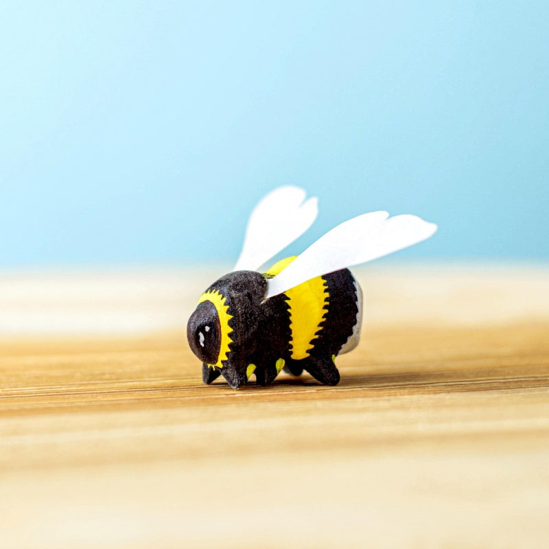 Toy bee with black and yellow stripes and white wings on a sandy surface with a blue sky.