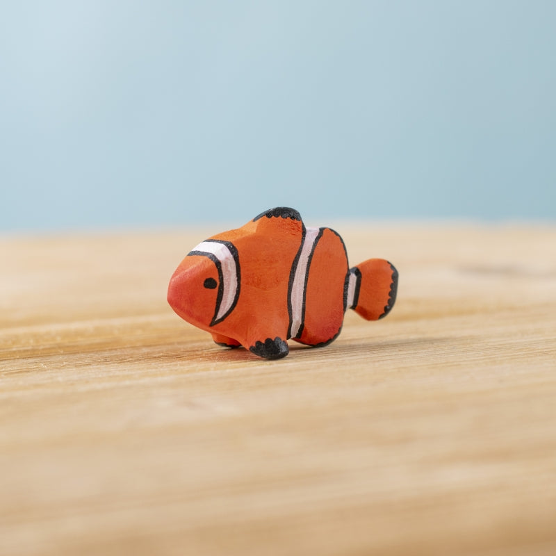 Plush toy fish resembling Nemo from 'Finding Nemo' on a wooden surface with a light blue background