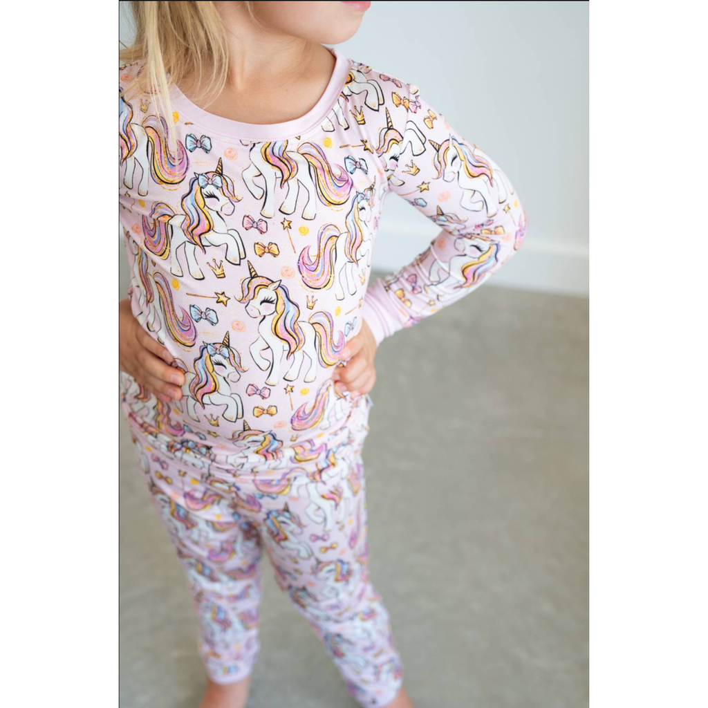 Child wearing a pink pajama set with a pattern of colorful characters on a plain background