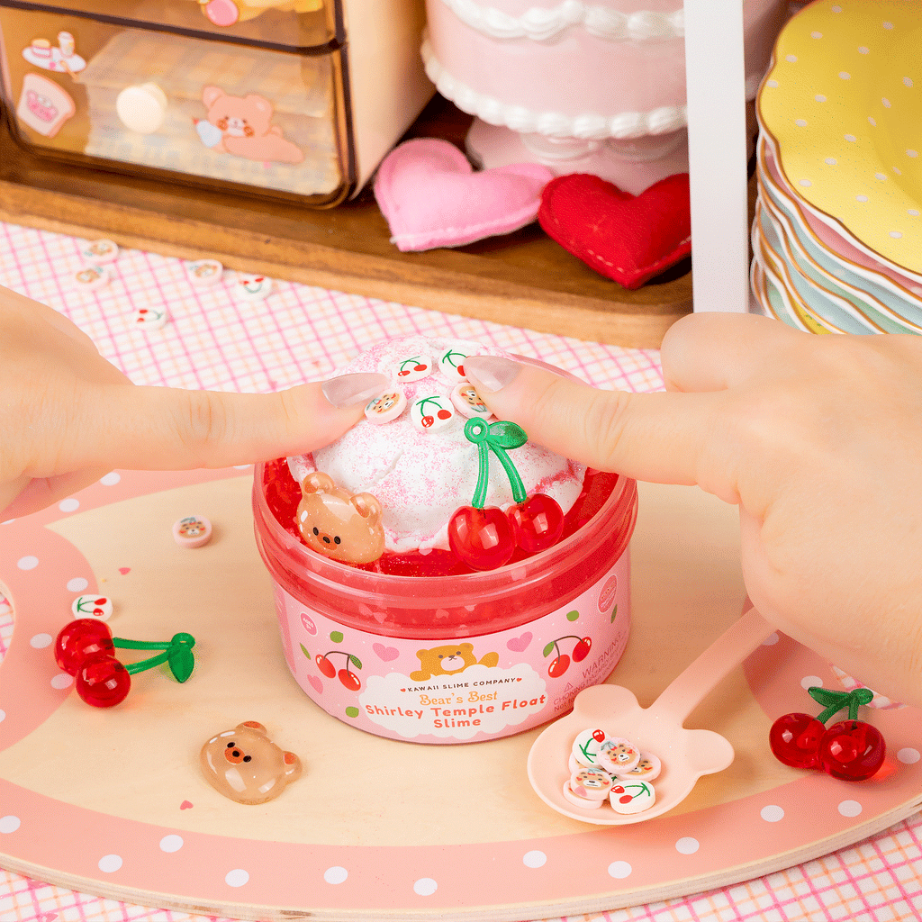 Kawaii Slime Company 'Seat's Bear Shirley Temple Float Slime' in a pink round container with a clear dome lid, decorated with a large red ribbon bow, cherry illustrations, and a white float filled with white slime, a brown bear figure, and red cherry charms.