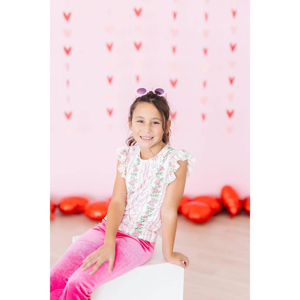 Child wearing a white shirt with pink floral and bow patterns and pink pants.