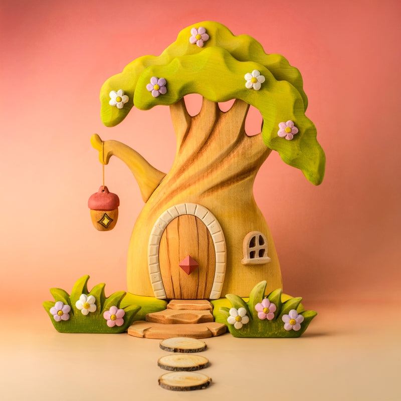 Wooden fairy house with a green roof and pink flowers on a light blue background