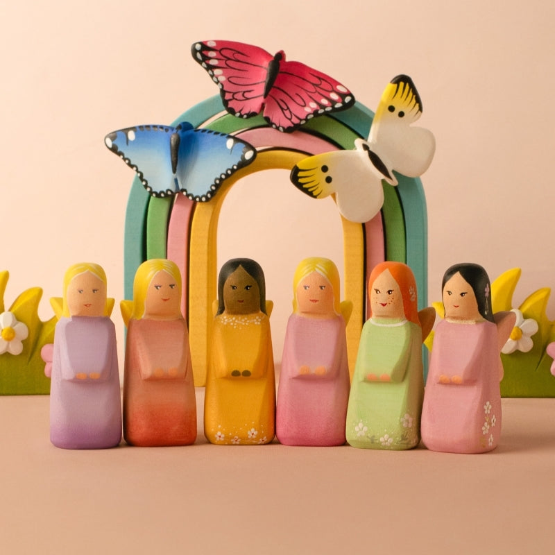 Small figurine of a person in a pink garment with floral patterns on a wooden surface and light blue background