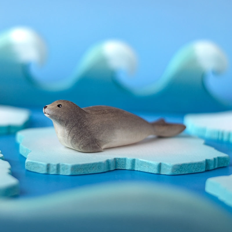 A small realistic seal figurine lying on a light wooden surface with a soft blue background.