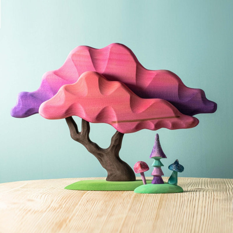 Hand holding a colorful tree-shaped object with a gradient from pink to purple against a light blue background.