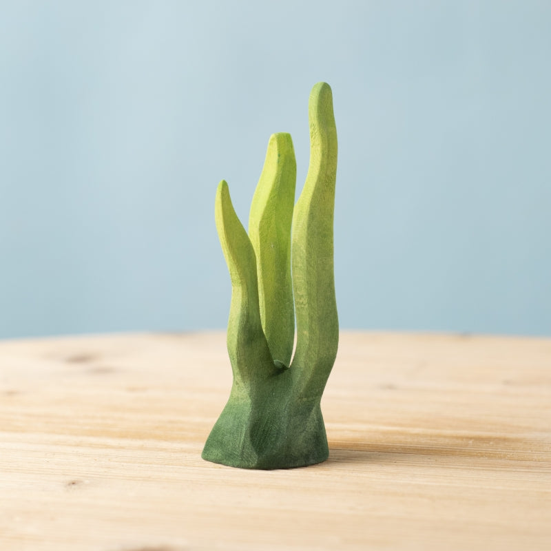 Green plant-like sculpture on a wooden surface with a light blue background