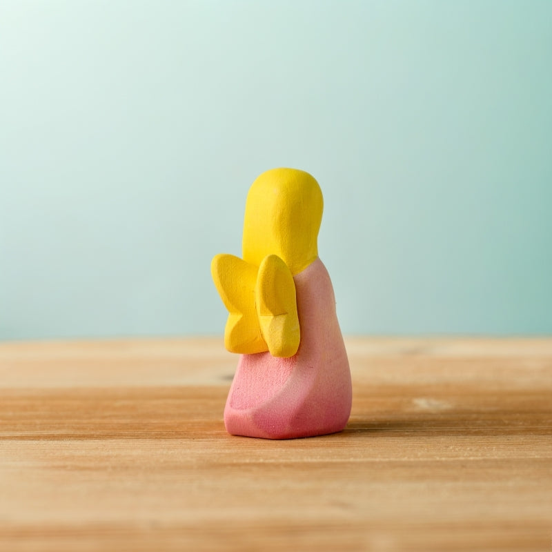 Small figurine of a person with yellow hair and pink body on a wooden surface with a light blue background