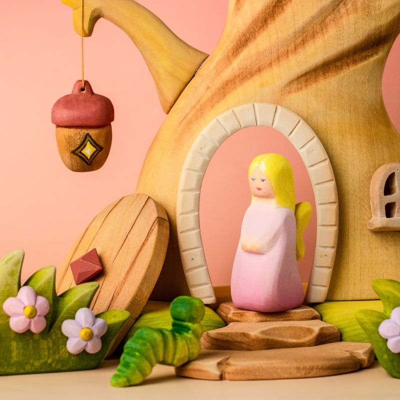 Wooden angel figurine with pink dress and yellow hair on a wooden surface with a light blue background