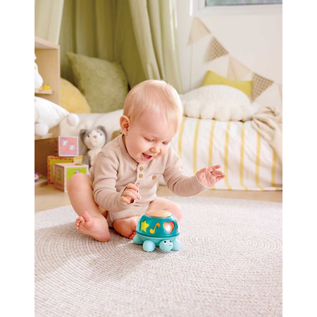 Child playing with a turtle-shaped toy drum on a carpeted floor.
